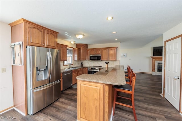 kitchen with a breakfast bar area, a peninsula, appliances with stainless steel finishes, and dark wood finished floors