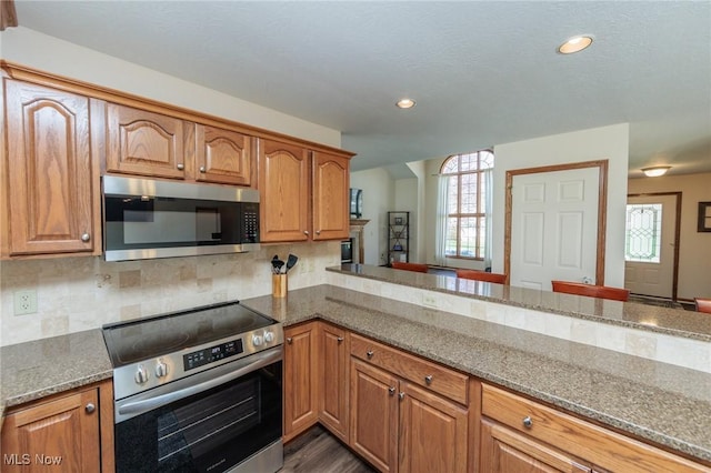 kitchen featuring dark stone counters, decorative backsplash, appliances with stainless steel finishes, recessed lighting, and brown cabinetry