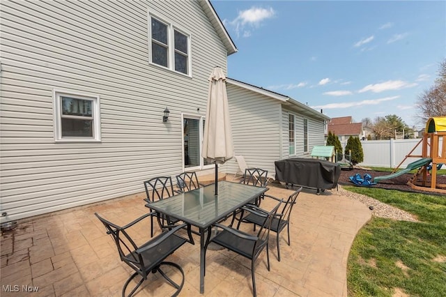 view of patio with outdoor dining area, a playground, and a fenced backyard