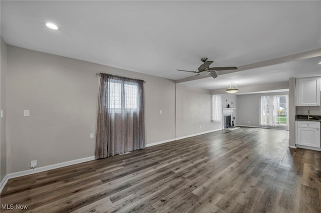 unfurnished living room with a fireplace, a ceiling fan, dark wood-type flooring, and baseboards