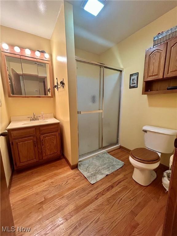 bathroom with a stall shower, wood finished floors, vanity, baseboards, and toilet