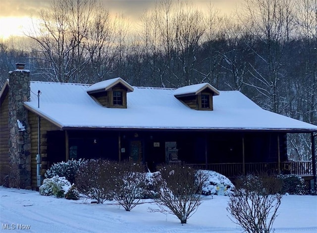 view of front of house with covered porch, log exterior, and a chimney