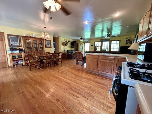 kitchen featuring a peninsula, light wood-style flooring, ceiling fan with notable chandelier, and range with gas cooktop