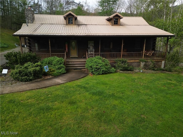 view of front of house with a chimney, covered porch, a front yard, and log siding