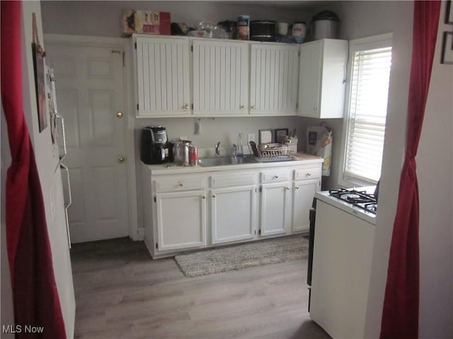 kitchen with light wood-style flooring, light countertops, white cabinets, a sink, and white range with gas stovetop