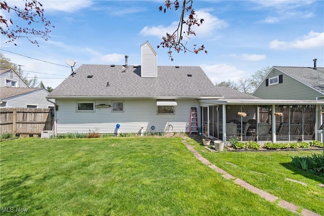 rear view of house featuring a sunroom, roof with shingles, a yard, and fence
