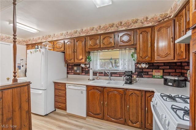 kitchen with light countertops, a sink, brown cabinets, and white appliances