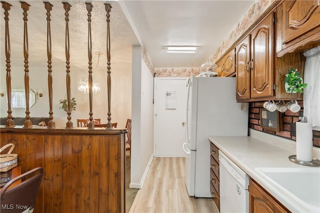 kitchen with brown cabinets, light wood-style flooring, a sink, light countertops, and white appliances