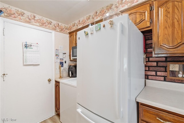 kitchen featuring washer / clothes dryer, brown cabinets, light countertops, and freestanding refrigerator