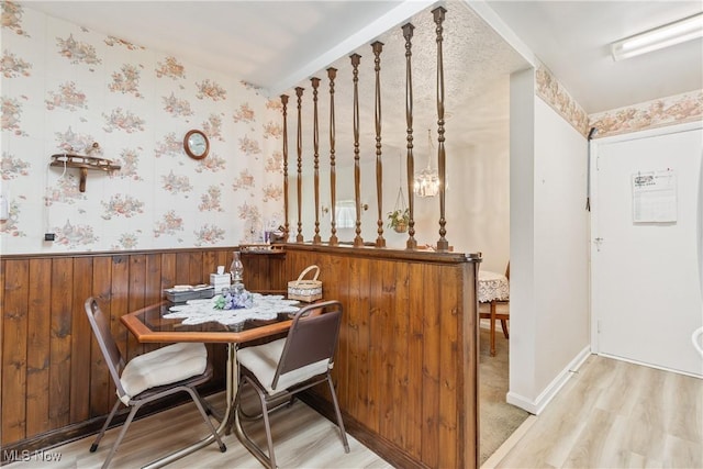 dining room with wainscoting, wood finished floors, wood walls, and wallpapered walls