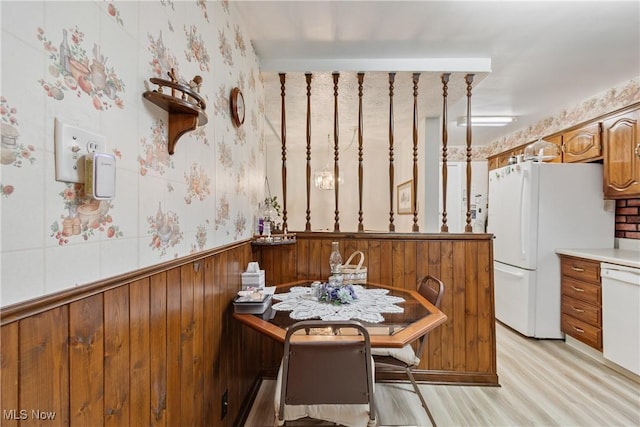 kitchen with white appliances, wallpapered walls, brown cabinetry, a wainscoted wall, and light wood-type flooring