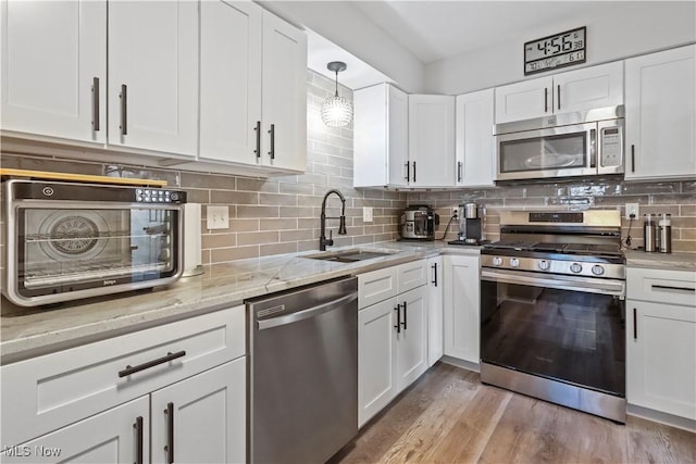 kitchen featuring appliances with stainless steel finishes, white cabinetry, decorative backsplash, and a sink