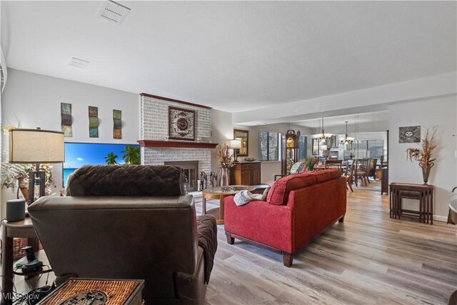 living room with a chandelier, visible vents, light wood-style flooring, and a brick fireplace