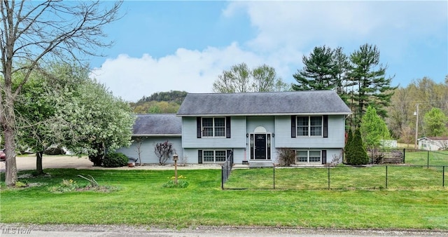 raised ranch featuring fence, a shingled roof, and a front yard