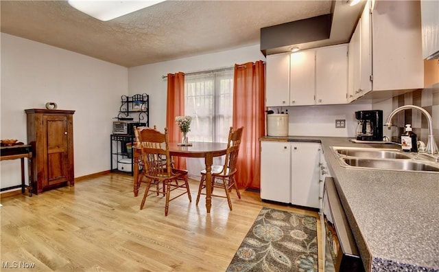 kitchen with a textured ceiling, light wood-style floors, white cabinets, and a sink