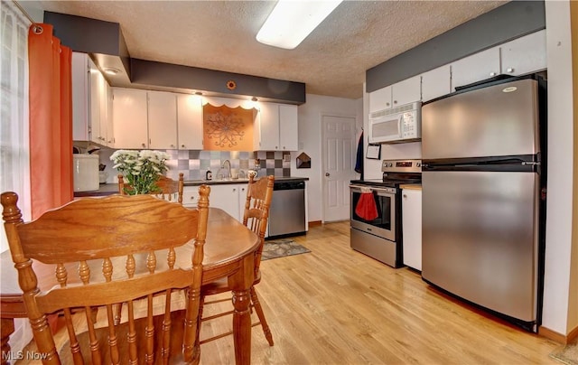 kitchen featuring light wood-style flooring, white cabinets, a sink, stainless steel appliances, and backsplash
