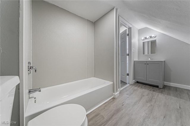 bathroom featuring baseboards, wood finished floors, a bath, and vaulted ceiling