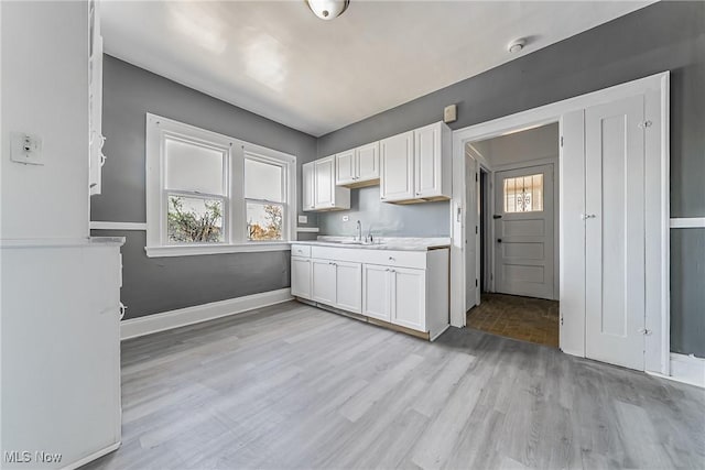 kitchen featuring light wood-style flooring, a sink, white cabinets, and a wealth of natural light