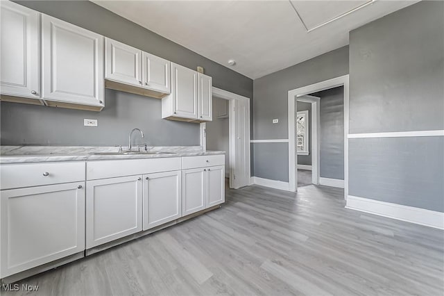 kitchen featuring white cabinetry, a sink, light wood-style floors, and baseboards