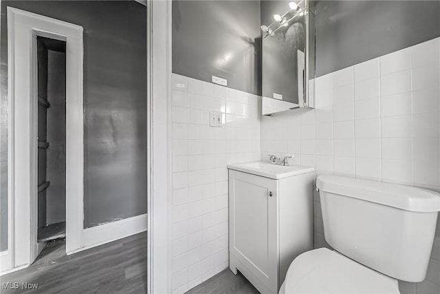 half bathroom featuring toilet, vanity, tile walls, and wood finished floors