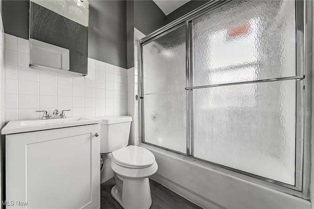 full bathroom featuring wood finished floors, combined bath / shower with glass door, tile walls, toilet, and vanity