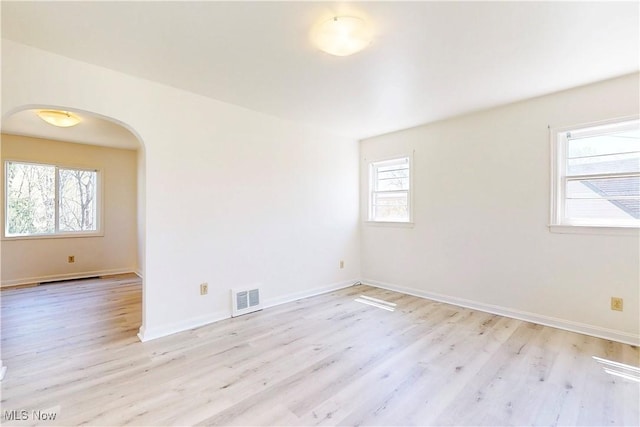 unfurnished room featuring arched walkways, visible vents, a wealth of natural light, and wood finished floors