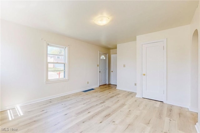 empty room featuring arched walkways, visible vents, light wood-style flooring, and baseboards