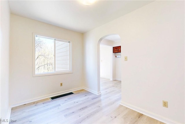 empty room with visible vents, light wood-style floors, baseboards, and arched walkways