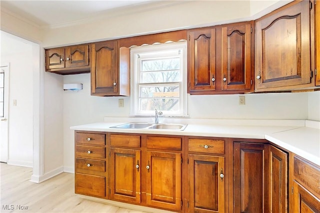 kitchen featuring brown cabinetry, light wood-style floors, light countertops, ornamental molding, and a sink