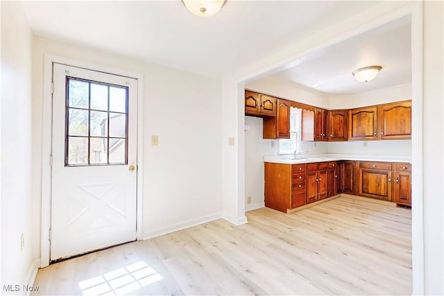 kitchen featuring baseboards, light countertops, light wood finished floors, and brown cabinets