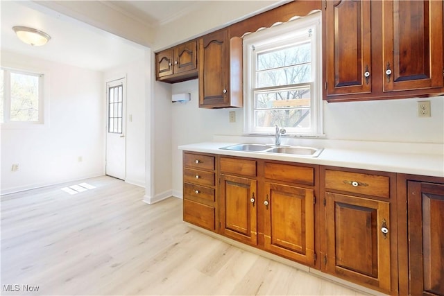 kitchen featuring light countertops, light wood finished floors, brown cabinetry, and a sink