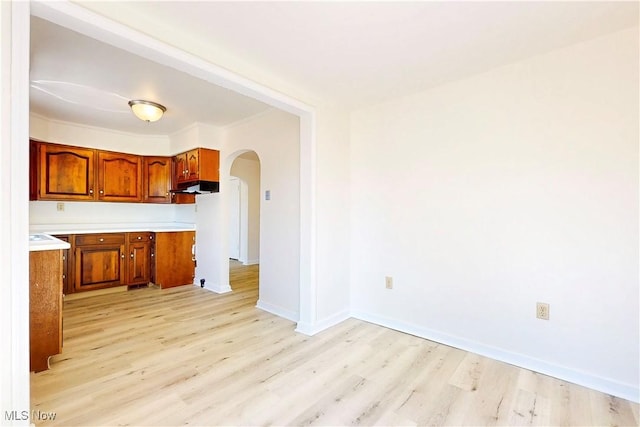 kitchen with arched walkways, light wood-style flooring, under cabinet range hood, light countertops, and brown cabinets