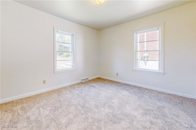 carpeted spare room with baseboards, visible vents, and plenty of natural light