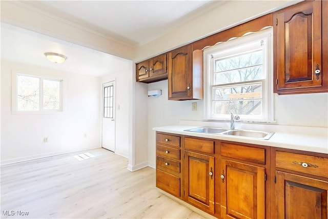 kitchen with a sink, light wood-style floors, brown cabinetry, and light countertops