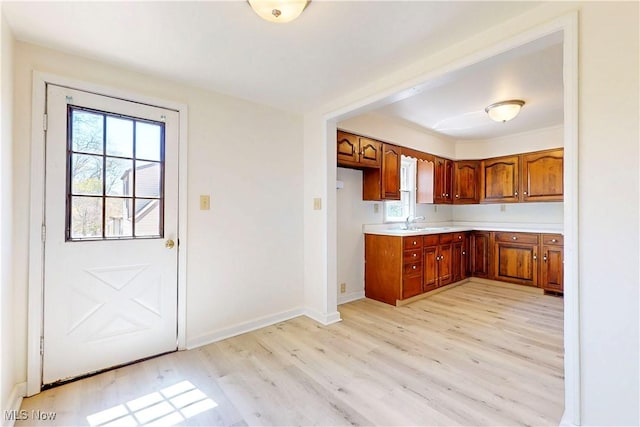 kitchen featuring a sink, light countertops, baseboards, light wood-type flooring, and brown cabinetry