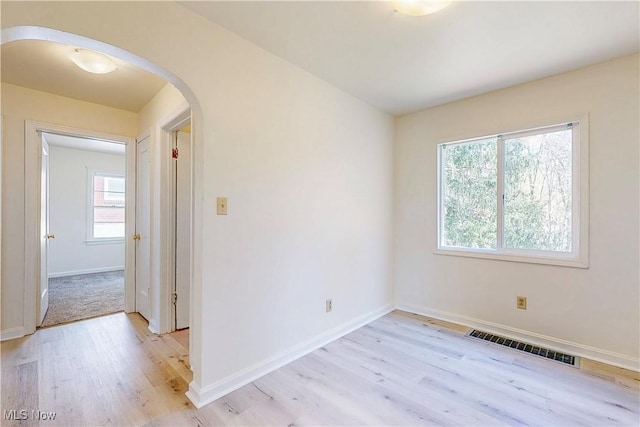 unfurnished room with light wood finished floors, arched walkways, visible vents, and baseboards