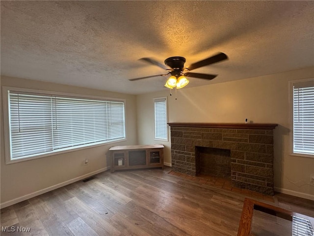 unfurnished living room with wood finished floors, ceiling fan, baseboards, visible vents, and a textured ceiling
