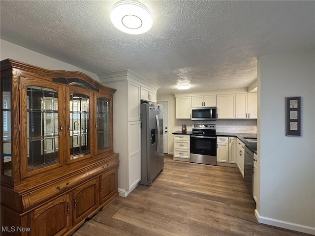 kitchen featuring dark wood-style floors, dark countertops, appliances with stainless steel finishes, and white cabinetry