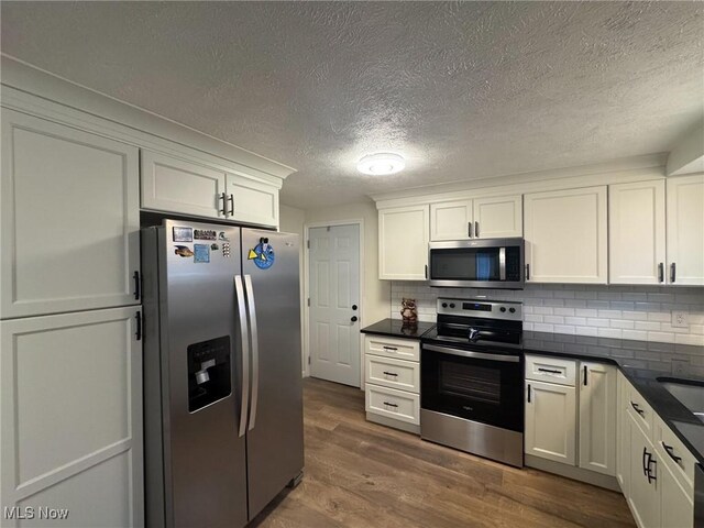 kitchen featuring tasteful backsplash, dark countertops, a textured ceiling, appliances with stainless steel finishes, and dark wood finished floors