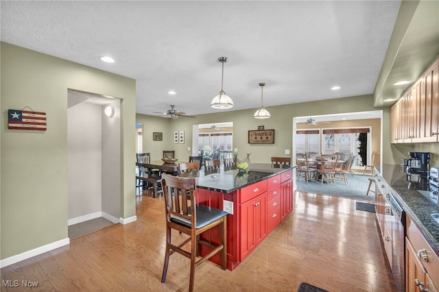 kitchen with a breakfast bar area, a ceiling fan, baseboards, and light wood-style floors