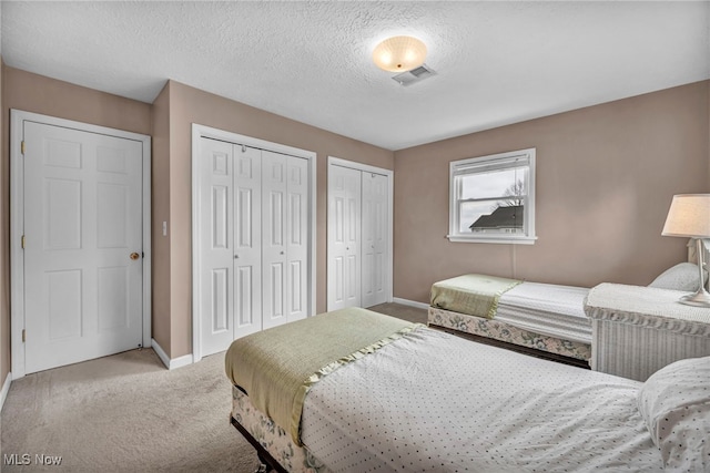 carpeted bedroom with baseboards, a textured ceiling, two closets, and visible vents