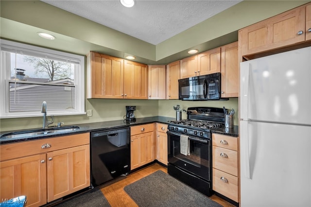 kitchen with a textured ceiling, light brown cabinetry, wood finished floors, a sink, and black appliances