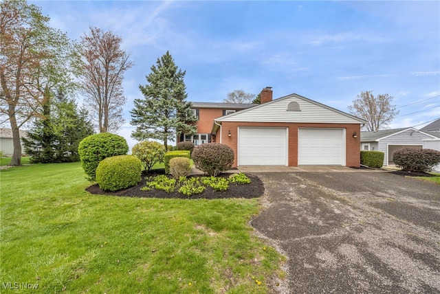 view of front of house featuring a garage, a front lawn, a chimney, brick siding, and driveway