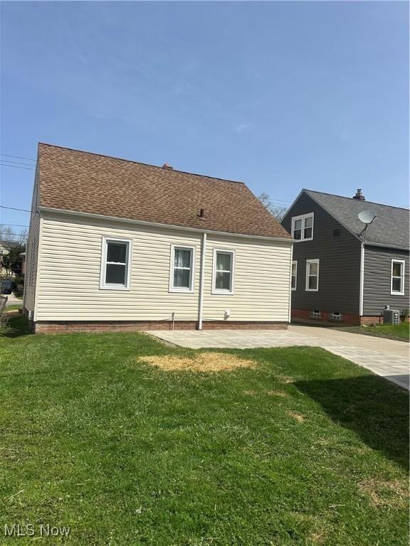 rear view of property featuring a yard, a patio area, and a shingled roof