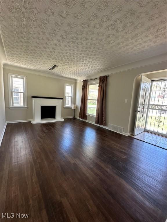 unfurnished living room featuring dark wood finished floors, arched walkways, a fireplace with raised hearth, baseboards, and visible vents