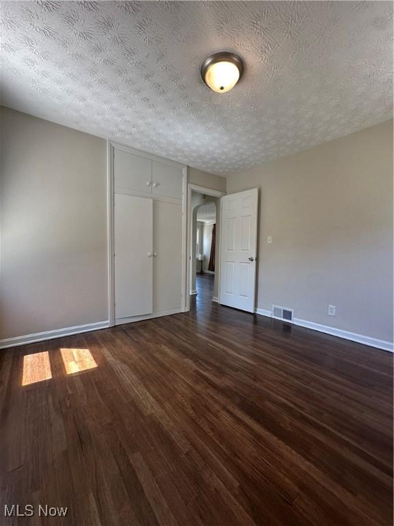 empty room featuring a textured ceiling, visible vents, arched walkways, baseboards, and dark wood-style flooring