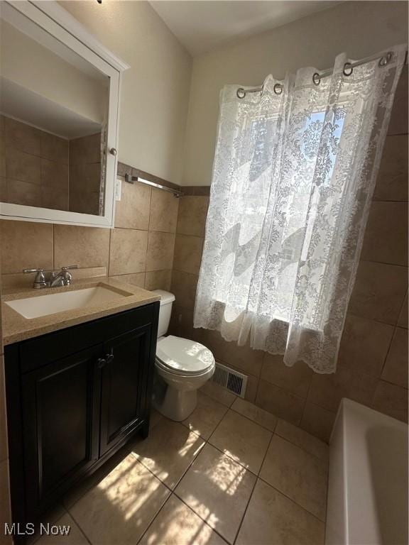 bathroom featuring a washtub, visible vents, toilet, tile walls, and vanity