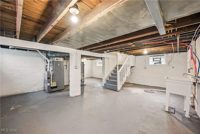 basement featuring heating unit, gas water heater, concrete block wall, a sink, and stairway