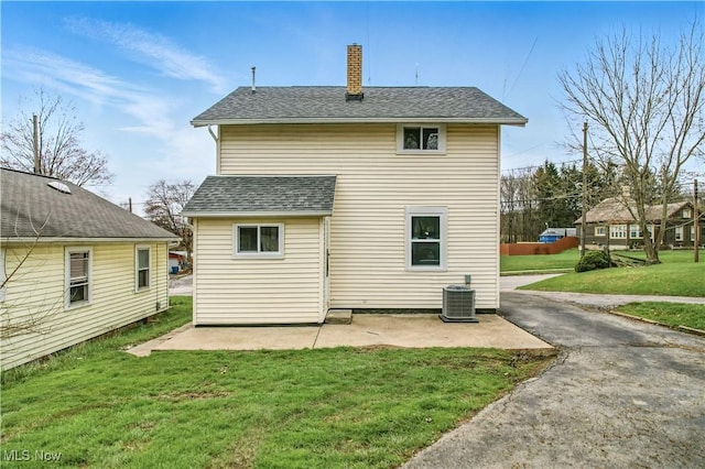 rear view of property with a shingled roof, a patio area, a yard, cooling unit, and a chimney