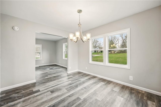 unfurnished dining area featuring wood finished floors, a chandelier, and baseboards